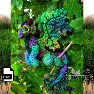 Puede incluir: Un dragón de crochet verde, morado y azul con cabeza y alas marrones. El dragón está sentado en una rama con hojas verdes.