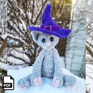 May include: A gray crocheted cat wearing a purple witch hat with a gold buckle. The cat is sitting in the snow.
