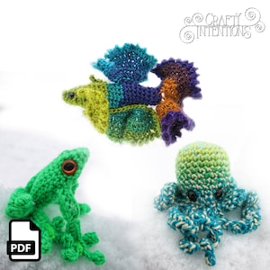 Könnte beinhalten: Ein Set aus drei gehäkelten Amigurumi-Spielzeugen: ein grüner Frosch, ein mehrfarbiger Fisch und ein blauer und grüner Oktopus. Die Spielzeuge liegen auf einer weißen Oberfläche. Crafty Intentions steht in einem Kreis in der oberen rechten Ecke des Bildes.