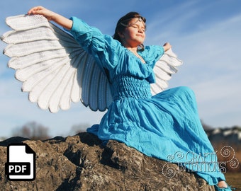 May include: A person wearing a blue dress and white crochet angel wings sits on a rock. The wings are spread wide against a blue sky. The image includes a PDF icon and the text "Crafty Intentions".
