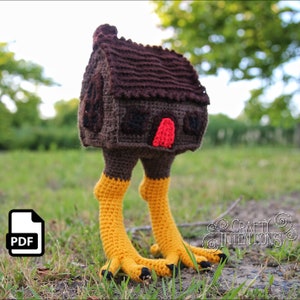May include: A crocheted house with a brown roof and yellow legs, standing on green grass. The house has a red door and black windows. The text "CRAFTY INTENTIONS" is visible in the lower right corner of the image.