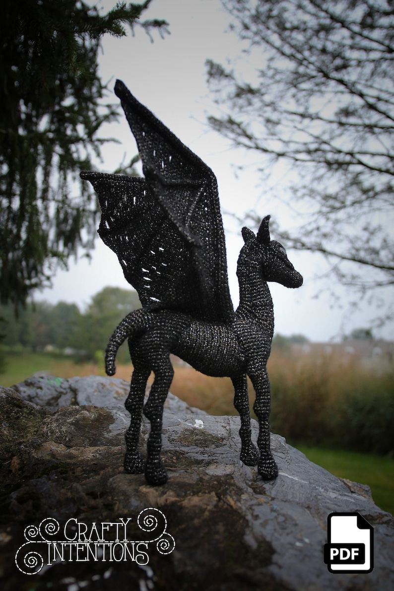May include: Black crocheted winged horse sculpture standing on a rock. The sculpture is made of black yarn and has a detailed design. The sculpture is a great addition to any home decor.