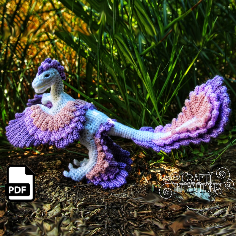 May include: Crochet pattern for a purple and pink dinosaur with a long tail and feathery wings. The pattern is available as a PDF download.