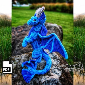 May include: A blue crocheted dragon with purple accents. The dragon has a long tail, wings, and a pointed horn on its head. The dragon is sitting on a rock.
