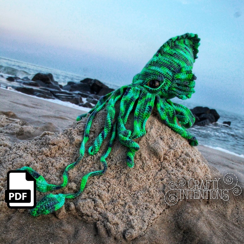 May include: A green and black crocheted squid amigurumi toy with large eyes, sitting on a sandy beach. The toy has long tentacles and is made with a striped pattern. The image includes the text "CRAFTY INTENTIONS" and a PDF icon.