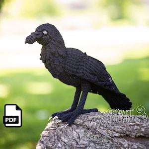 Op de afbeelding: Een handgemaakte zwarte gehaakte kraai met gedetailleerde veren en scherpe klauwen. De vogel zit op een verweerde rots, met een PDF-pictogram in de linkerbenedenhoek. Het oog van de kraai is een reflecterende kraal.