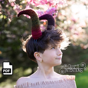 Puede incluir: Un patrón PDF para tejer al crochet un par de cuernos coloridos. Los cuernos están hechos con un hilo degradado en tonos rojos, naranjas, amarillos y verdes. Los cuernos están unidos a una diadema negra.