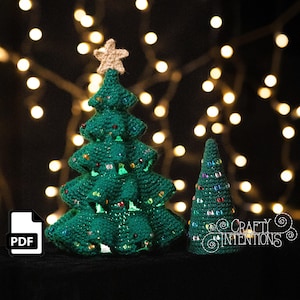 May include: Two green crocheted Christmas trees with colorful bead embellishments. The larger tree has a tan star on top. The background features blurred string lights. The image includes a PDF icon and the text "Crafty Intentions".
