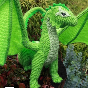 K&ouml;nnte beinhalten: Ein gr&uuml;ner geh&auml;kelter Drache mit Fl&uuml;geln, der auf einem Baumstumpf steht. Der Drache hat ein detailliertes Gesicht und einen strukturierten K&ouml;rper.