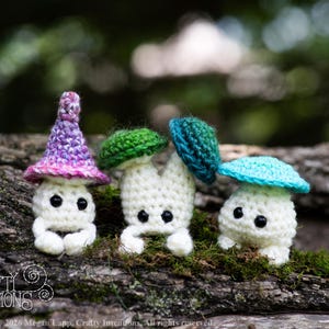 Puede incluir: Tres figuras de setas de ganchillo con cuerpos blancos y gorros coloridos en morado, verde y turquesa. Las figuras tienen ojos negros y est&aacute;n posadas sobre un tronco cubierto de musgo. La imagen incluye el texto "Crafty Intentions" y un icono PDF.