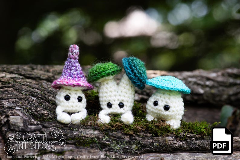 Puede incluir: Tres figuras de setas de ganchillo con cuerpos blancos y gorros coloridos en morado, verde y turquesa. Las figuras tienen ojos negros y est&aacute;n posadas sobre un tronco cubierto de musgo. La imagen incluye el texto "Crafty Intentions" y un icono PDF.