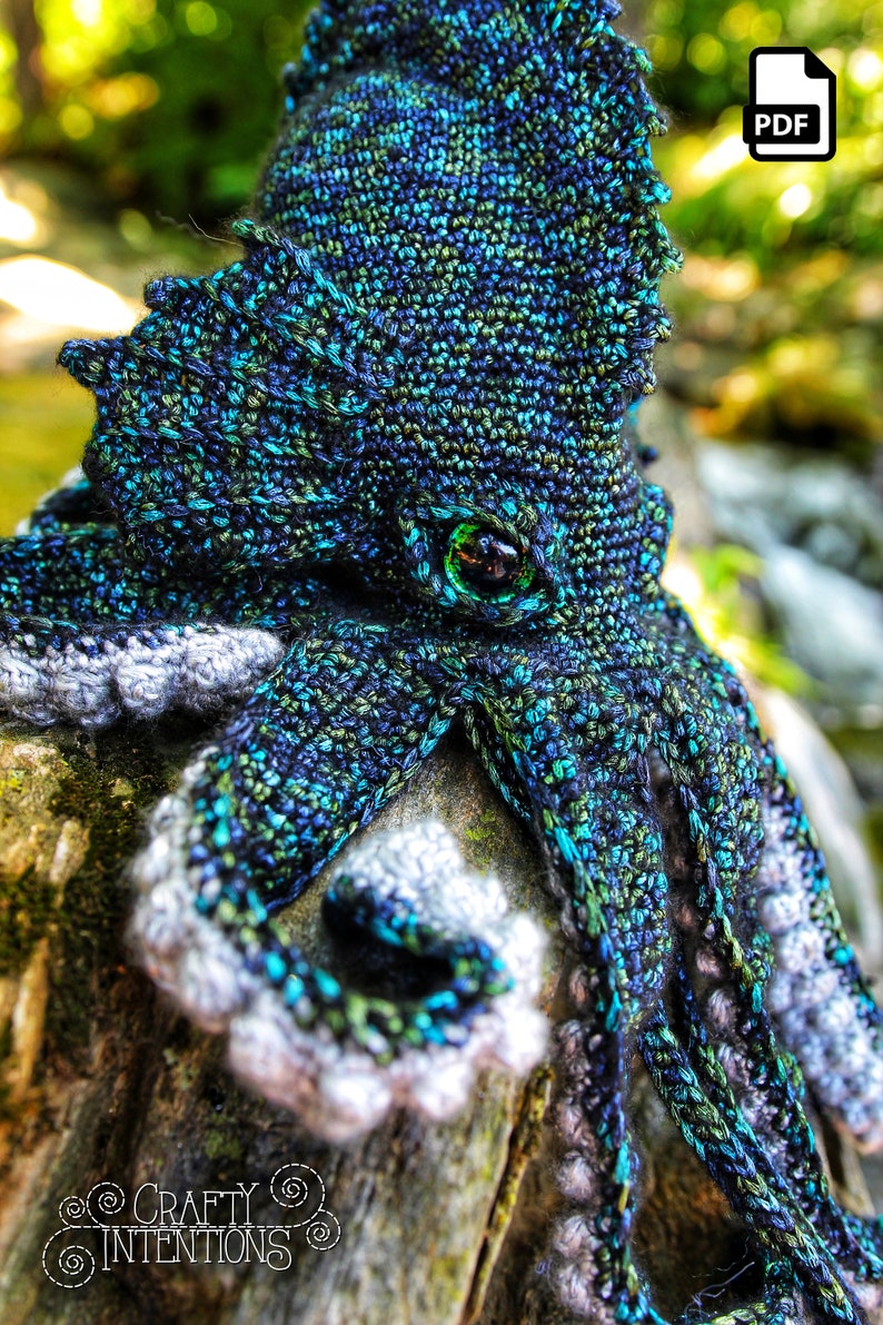 May include: A crocheted octopus amigurumi toy with a green eye, blue, green, and black yarn, and a gray and white yarn for the tentacles. The octopus is sitting on a piece of wood.