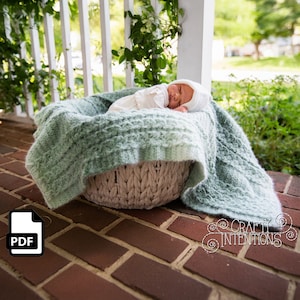 May include: A baby sleeping in a woven basket lined with a soft, green blanket. The basket is sitting on a brick patio.