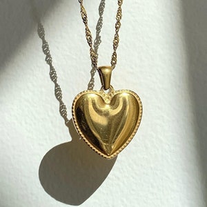 Könnte beinhalten: Eine goldene Kettenkette mit einem herzförmigen Anhänger. Der Anhänger hat eine strukturierte Oberfläche und einen leicht erhöhten Rand.