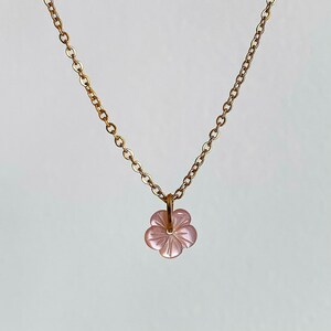May include: A delicate gold chain necklace with a pink flower pendant. The flower is carved from shell and has a detailed design.