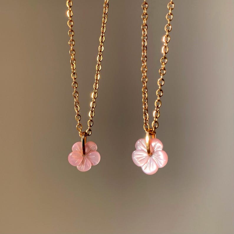 May include: Two gold necklaces with pink flower pendants. The necklaces are delicate and feminine.