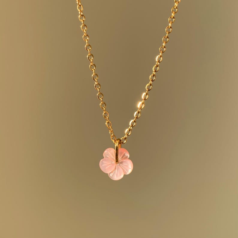 May include: A delicate gold chain necklace with a pink flower pendant.