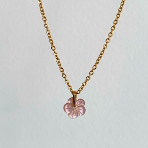 May include: A delicate gold chain necklace with a pink flower pendant. The flower is carved from a translucent material and has a delicate, feminine design.