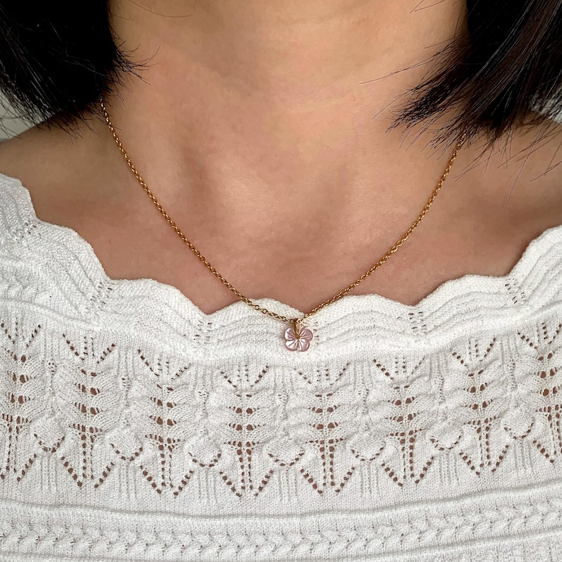 May include: A gold chain necklace with a small pink flower pendant.