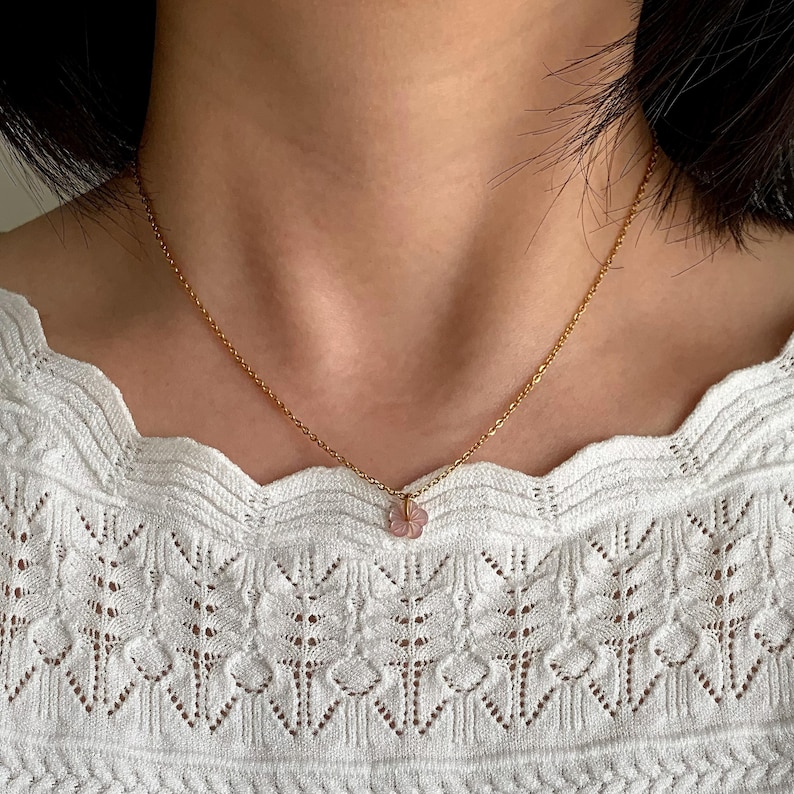 May include: A delicate gold chain necklace with a small pink flower pendant.