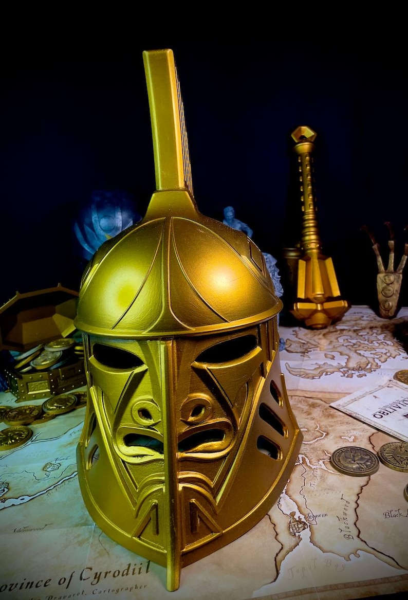 K&ouml;nnte beinhalten: Ein goldfarbener Helm mit einem hohen, rechteckigen Oberteil und einem detaillierten Gesichtsdesign. Der Helm ist Teil einer Sammlung von Fantasy-Artikeln, darunter ein Streitkolben, M&uuml;nzen und eine Schatztruhe, die alle auf einer Karte ausgestellt sind.