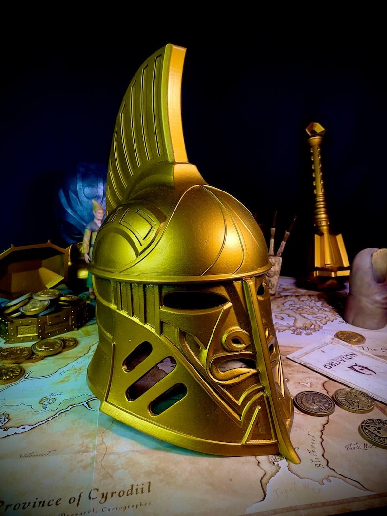 K&ouml;nnte beinhalten: Ein goldfarbener Helm mit hohem, vertikalem Kamm und aufwendigen Details. Der Helm hat Augen- und Mund&ouml;ffnungen und wird auf einer Karte mit M&uuml;nzen und einer Schatztruhe ausgestellt. Das Gesamtthema ist Fantasy oder Historie.