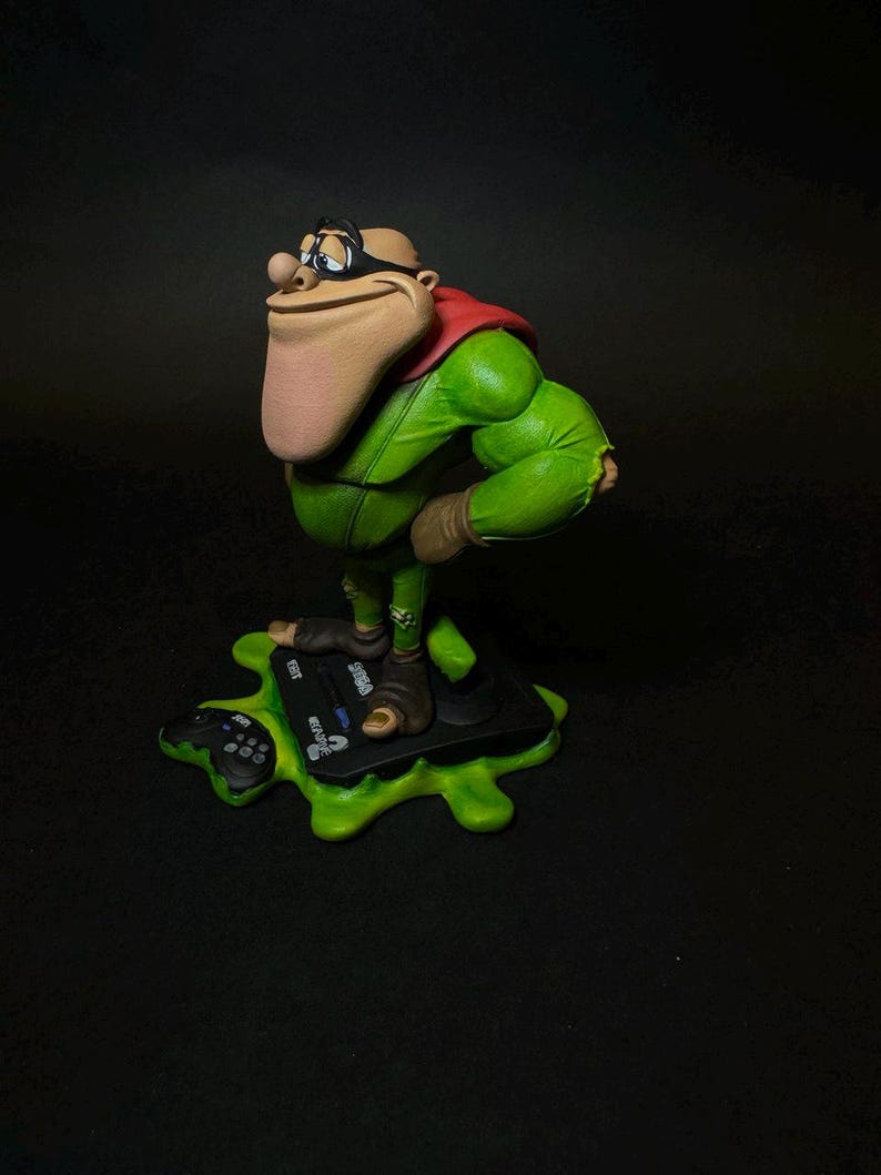 K&ouml;nnte beinhalten: Detaillierte Figur einer Zeichentrickfigur in einem gr&uuml;nen Outfit mit rotem Umhang und schwarzer Brille. Die Figur steht auf einer schwarzen Plattform mit gr&uuml;nem, gesprenkeltem Sockel. Die Figur hat eine gro&szlig;e Nase und einen selbstbewussten Ausdruck.