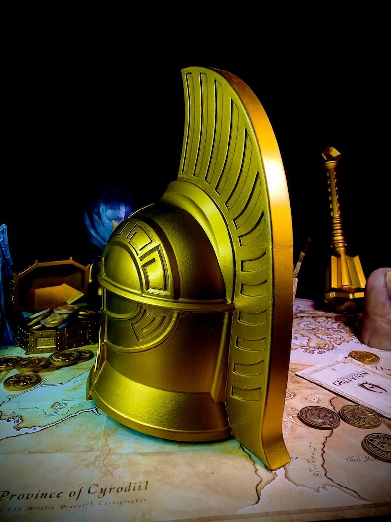 K&ouml;nnte beinhalten: Ein goldener Helm mit hohem, verziertem Kamm vor dunklem Hintergrund. Der Helm weist detaillierte Rillen und geometrische Muster auf. Eine Karte und M&uuml;nzen im Hintergrund deuten auf ein Fantasy- oder historisches Thema hin.