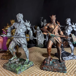 Op de afbeelding: Een verzameling fantasiebeeldjes, waaronder twee prominente beelden van gespierde figuren met wapens. De beelden zijn geschilderd in grijstinten, brons en groen, staand op getextureerde bases. Andere beeldjes zijn zichtbaar op de achtergrond.