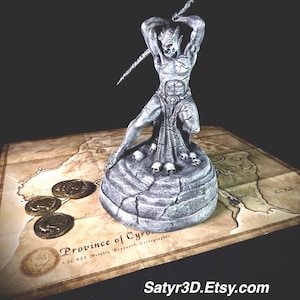 May include: A gray stone-textured figurine of a horned humanoid creature holding a spear above its head, standing on a circular base decorated with small skulls. Three metallic coins lie nearby on a map labeled Province of Cyrodiil.