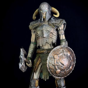 Op de afbeelding: Gedetailleerd beeldje van een skeletkrijger in sierlijke bepantsering, met een strijdbijl en een rond schild. De figuur heeft een gehoornde helm en is geschilderd in tinten zilver, brons en groen. De achtergrond is zwart.