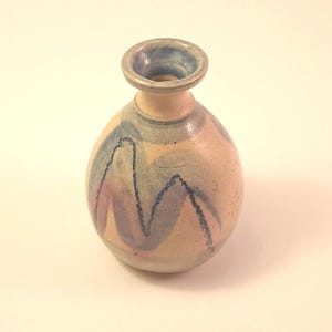 May include: A handmade ceramic vase with a rounded body and a narrow neck. The vase is painted with a beige base color and features abstract wavy designs in blue, purple, and gray. The rim of the vase is a darker blue.
