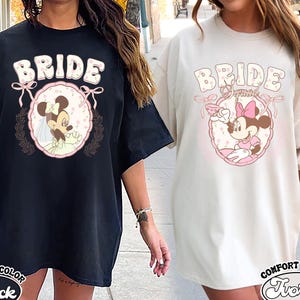 May include: Two black and white t-shirts with a bride and Mickey Mouse graphic. The text on the shirts says "Bride". One shirt is black and the other is ivory.