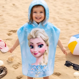 Puede incluir: Toalla de playa con capucha azul claro con un dise&ntilde;o de Elsa de Frozen y el nombre "JESSICA". Un ni&ntilde;o lleva la toalla en una playa de arena, con chanclas, un bal&oacute;n de playa y gafas de sol.