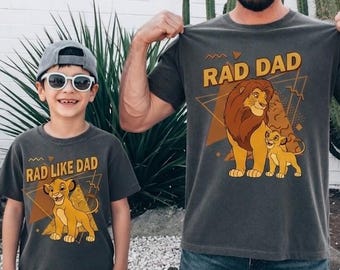May include: Two charcoal gray t-shirts with matching graphics. One shirt says "RAD DAD" with a lion family design. The other says "RAD LIKE DAD" with a similar lion cub design. Both shirts are short-sleeved.