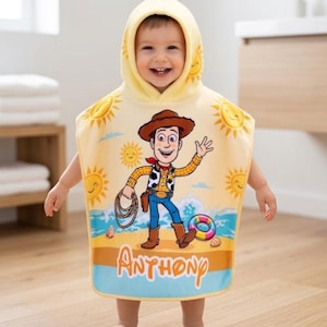 Puede incluir: Una toalla de playa con capucha amarilla con una imagen de dibujos animados de Woody de Toy Story, con gr&aacute;ficos de sol y playa. La toalla tiene el nombre "Anthony" impreso en la parte inferior. El ni&ntilde;o lleva la toalla.