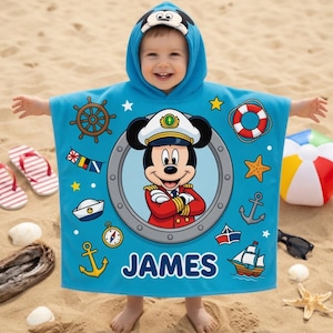 Op de afbeelding: Een lichtblauwe strandponcho met een Mickey Mouse kapitein ontwerp. De poncho is versierd met nautische symbolen zoals ankers, een scheepsstuur en een reddingsboei. De naam "JAMES" staat op de poncho. Perfect voor kinderen.