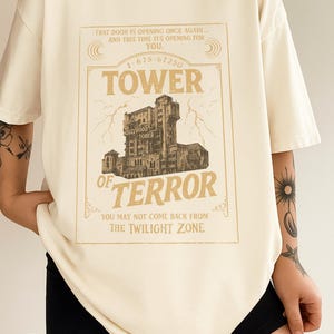 May include: Ivory t-shirt with a vintage-style graphic of the Hollywood Tower of Terror. The design includes the text "TOWER OF TERROR" and "YOU MAY NOT COME BACK FROM THE TWILIGHT ZONE."