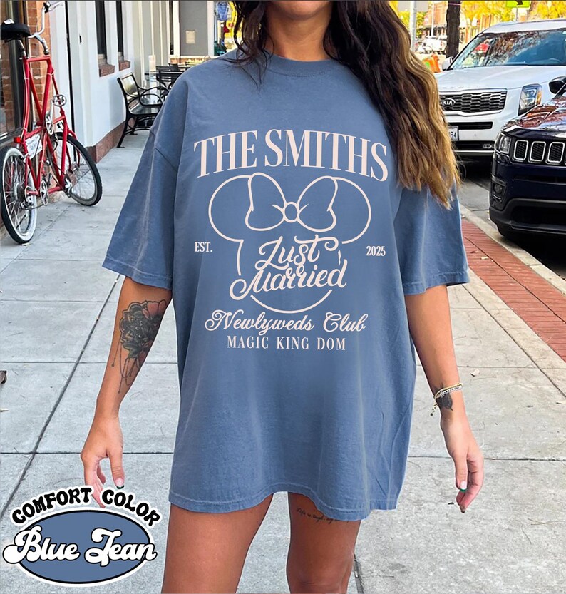 May include: Blue jean comfort color t-shirt with the text "THE SMITHS" and "Just Married" in white. The shirt also features a Mickey Mouse bow design and the words "Newlyweds Club" and "MAGIC KING DOM".