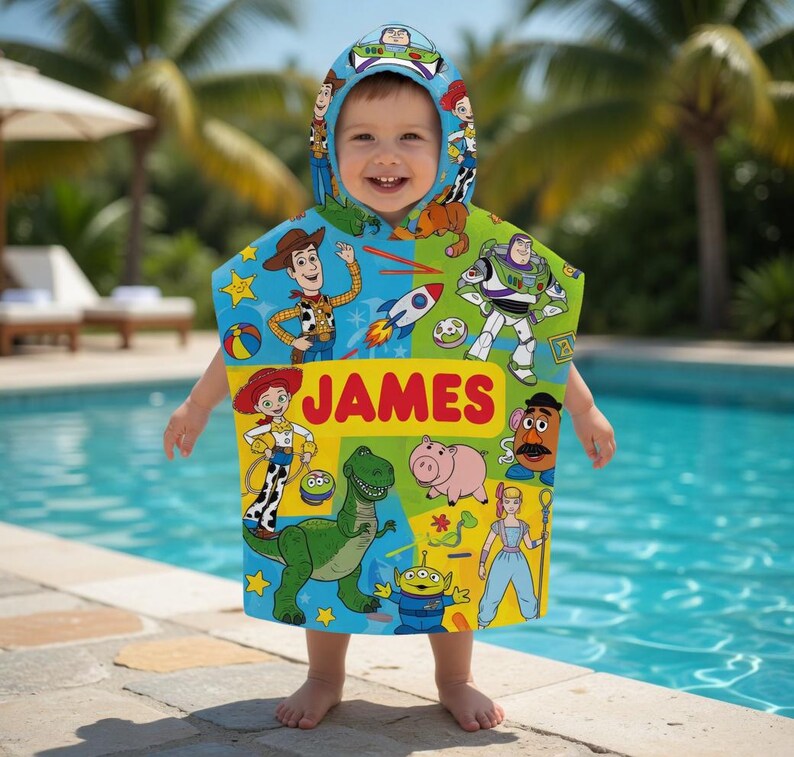 Puede incluir: Un ni&ntilde;o lleva una colorida toalla con capucha con personajes de la pel&iacute;cula Toy Story. La toalla es principalmente azul, verde y amarilla, con el nombre "JAMES" en letras rojas grandes. El fondo muestra una piscina y palmeras.
