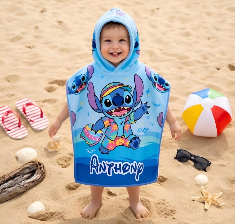 Puede incluir: Una toalla de playa con capucha azul claro con un dise&ntilde;o de personaje de dibujos animados. La toalla tiene un borde azul con el nombre "Anthony" impreso. La imagen tambi&eacute;n incluye un bal&oacute;n de playa, gafas de sol y chanclas.