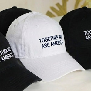 May include: A collection of baseball caps in black and white. Each cap has the phrase "TOGETHER WE ARE AMERICA" embroidered in a contrasting color. The caps are arranged in a row, showcasing the design.