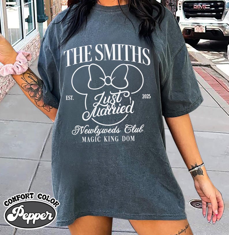May include: A gray Comfort Colors t-shirt with the text "THE SMITHS" and "Just Married" in white. The design includes a Mickey Mouse head silhouette and the words "Newlyweds Club" and "MAGIC KING DOM". The year "2025" is also printed on the shirt.