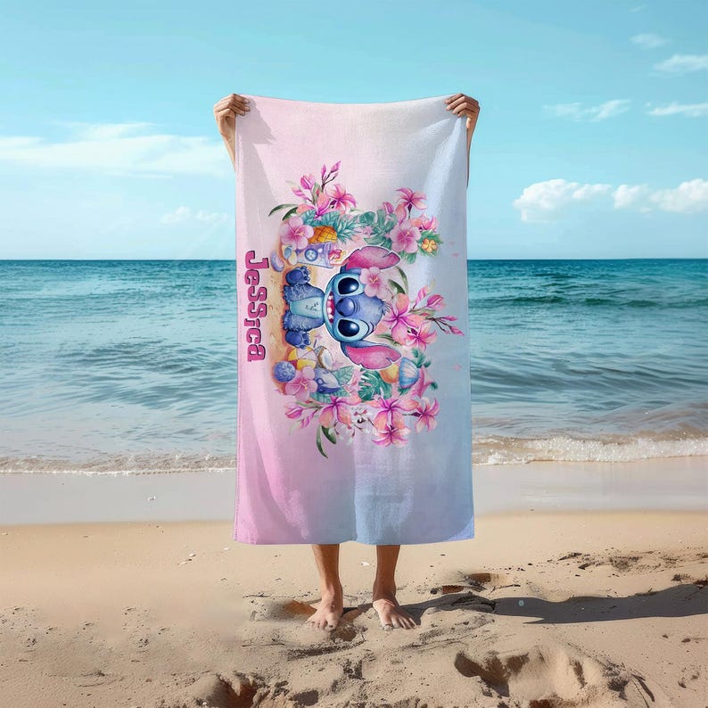 May include: A pink and blue beach towel with a cartoon Stitch character holding a tropical drink. The towel has a floral design and the name "Jessica" is printed on the side.