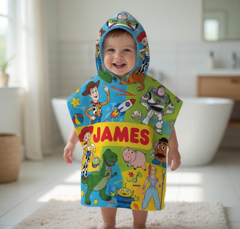 Puede incluir: Una toalla con capucha y colorida con personajes de Toy Story. La toalla es azul, verde y amarilla, con el nombre "JAMES" impreso en letras rojas grandes.