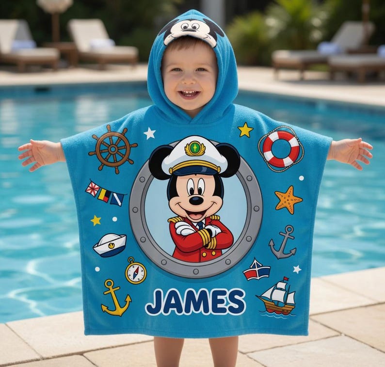 Op de afbeelding: Een blauwe badponcho met een Mickey Mouse-ontwerp. De poncho heeft nautische afbeeldingen, waaronder een scheepsstuur, anker en reddingsboei. De naam "JAMES" is in witte blokletters op de poncho gedrukt.