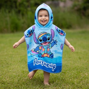 Puede incluir: Una toalla de playa con capucha azul claro con un personaje de dibujos animados, Stitch, con una camisa hawaiana. La toalla tiene un patr&oacute;n de olas azules y blancas y el nombre "Anthony" en escritura blanca. El ni&ntilde;o lleva la toalla y sonr&iacute;e.