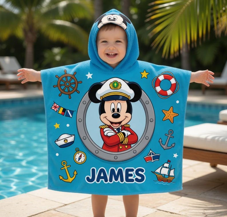 Op de afbeelding: Een lichtblauwe strandhanddoek met capuchon met een cartoon Mickey Mouse kapitein ontwerp. De handdoek heeft nautische thema graphics, waaronder een scheepsstuur, ankers en een zeilboot. De naam "JAMES" is op de handdoek gedrukt.