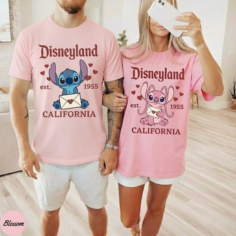 Op de afbeelding: Twee bijpassende roze t-shirts met het Disneyland-logo en een stripfiguur met een envelop. De shirts hebben ook de tekst "est. 1955 CALIFORNIA".