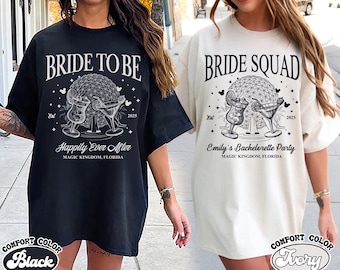 May include: Two white t-shirts with black text and graphics. The first shirt says "Bride to Be" with a graphic of a castle and two glasses of champagne. The second shirt says "Bride Squad" with a graphic of a castle and two glasses of champagne. Both shirts have the text "Est 2025" and "Magic Kingdom, Florida".